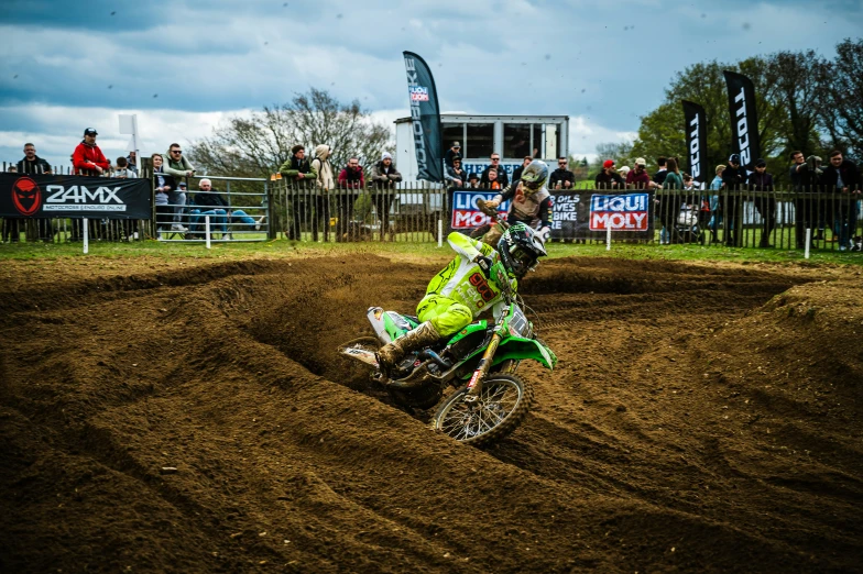 man with helmet and green suit on motorcycle on dirt track