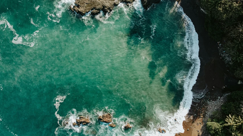 aerial view of green water waves breaking on rocky coast