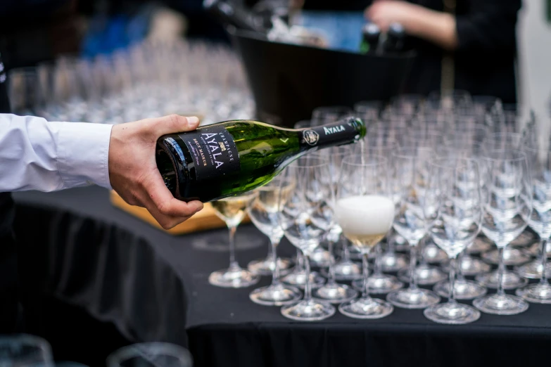 someone pouring wine into many wine glasses in front of an assortment of wine