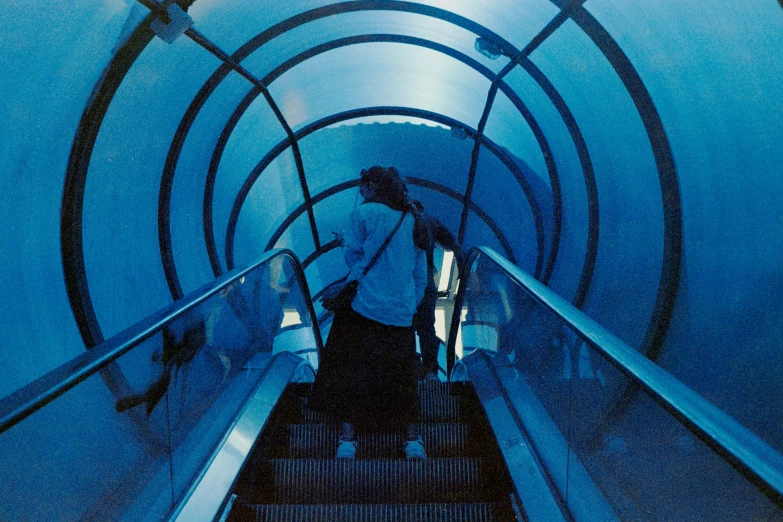 people walking down an escalator inside a blue tunnel