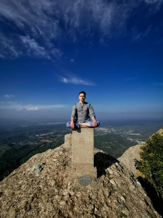 a man posing on a stone wall on top of a hill