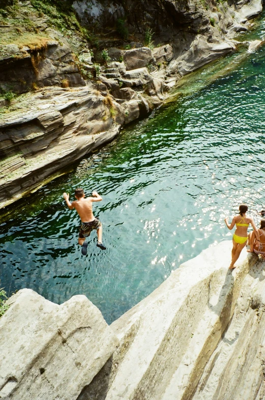 a group of people diving from the rocks into the water