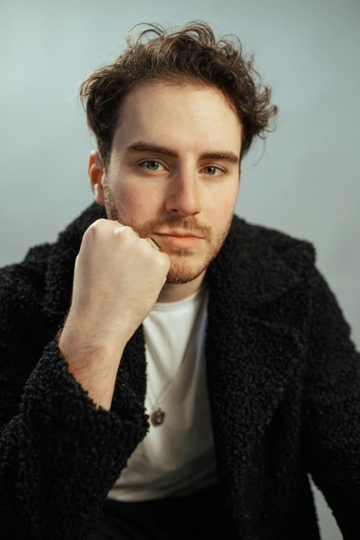 young man with beard sitting with hand on chin