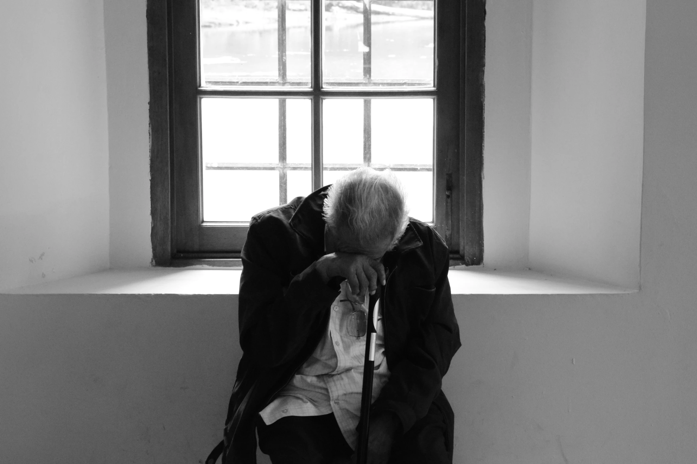 an old man with his head in his hands near the window