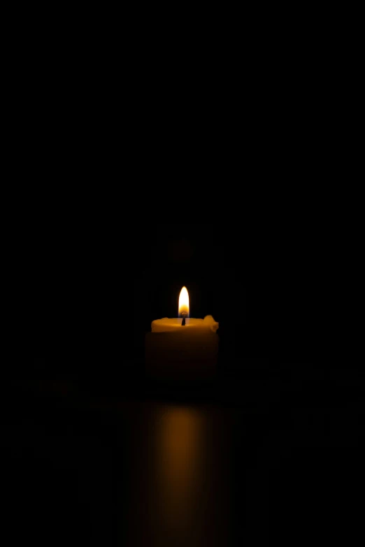 a lit candle in the dark with a light shining