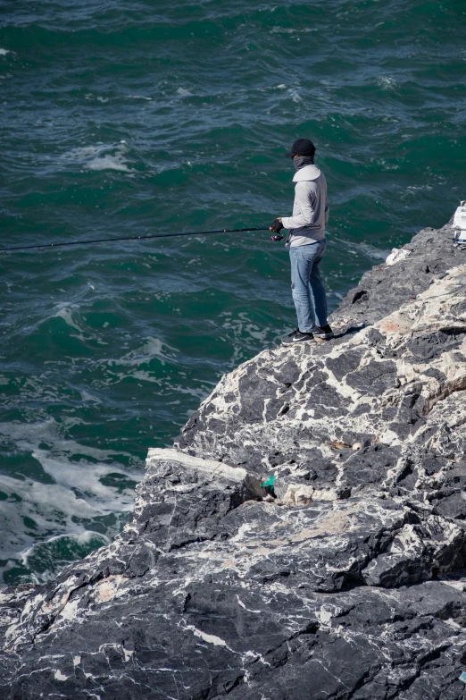 a man standing on a rock fishing in the ocean