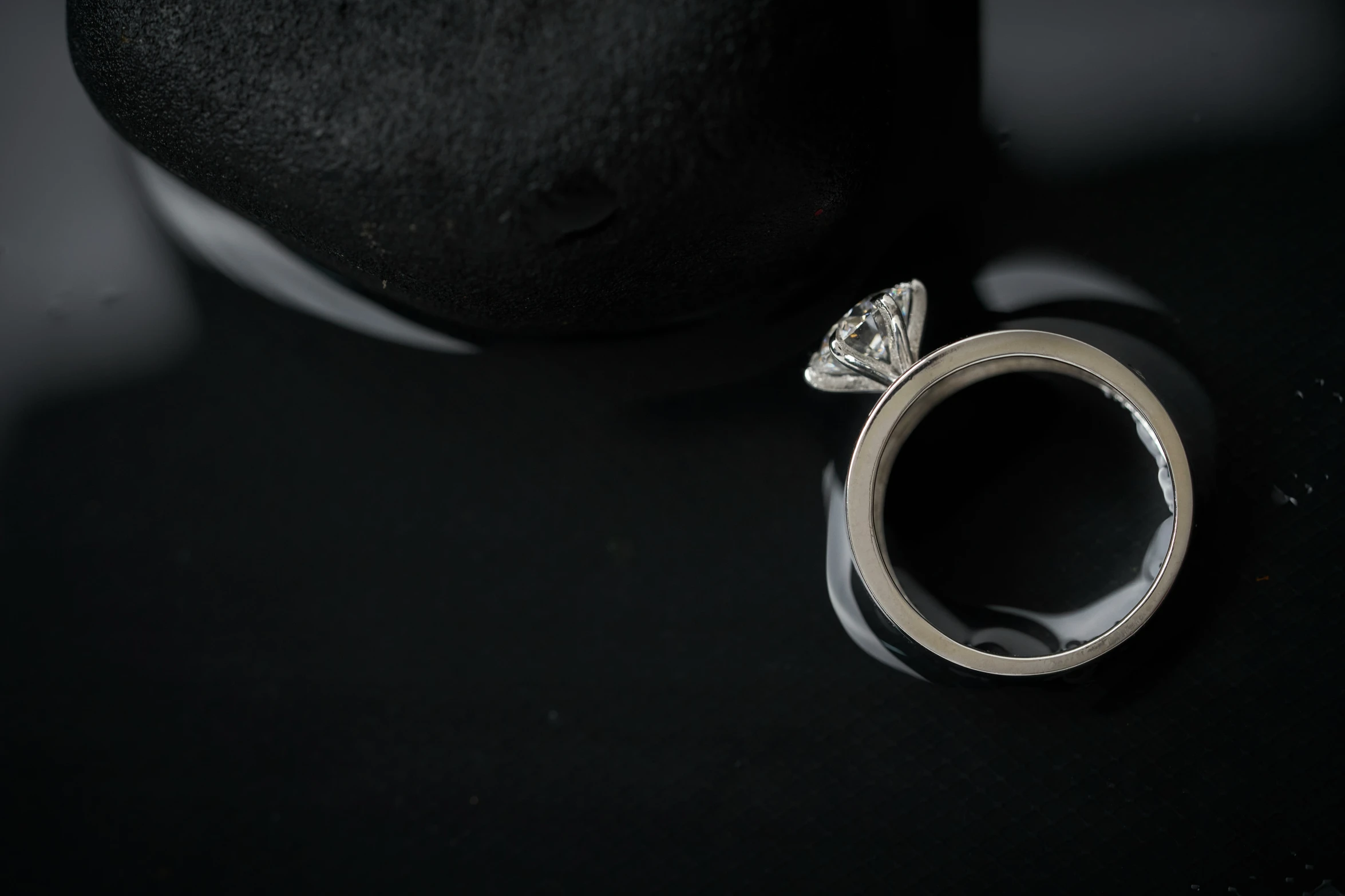 a silver ring with a diamond on a black surface