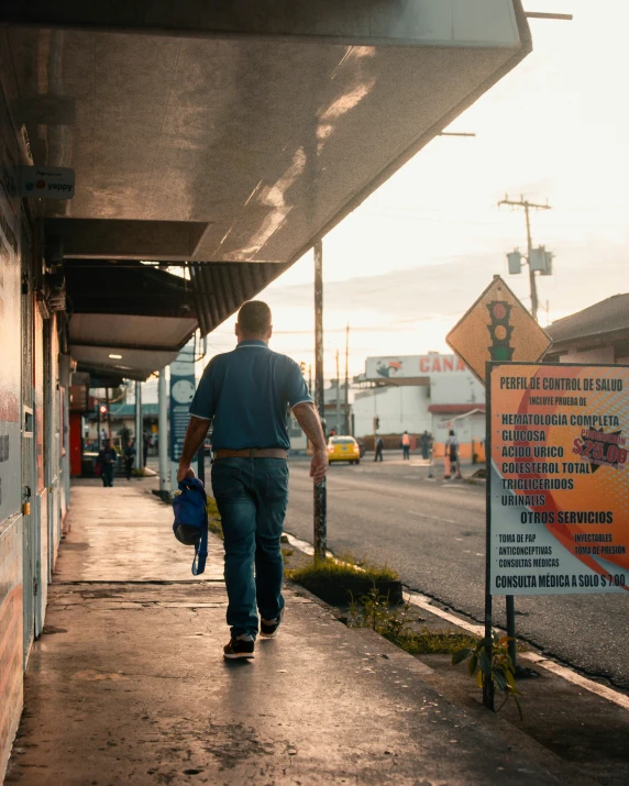 a man is walking down a side walk with a bag and suitcase