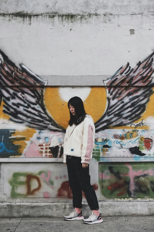 a young lady wearing black pants and a white jacket and a wall with colorful graffiti