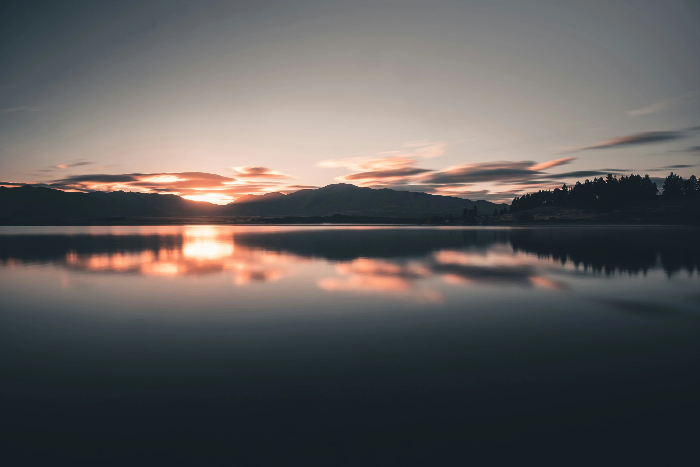 a lake surrounded by trees and mountains at sunset