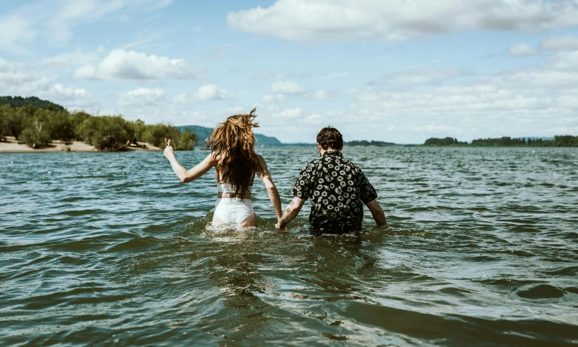 a man and a woman wade through water, holding hands