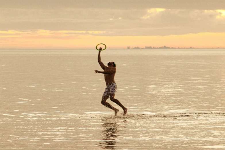 man in swim trunks catches a frisbee as he wades out into the water