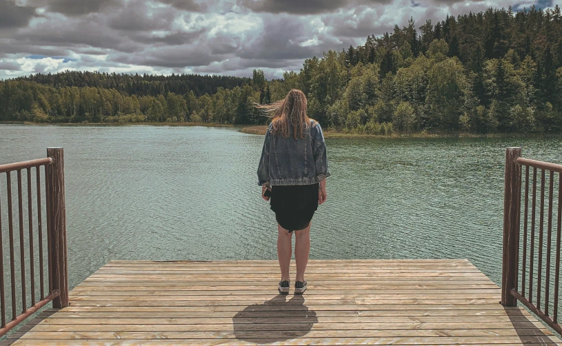 woman standing on dock over looking water near forested area