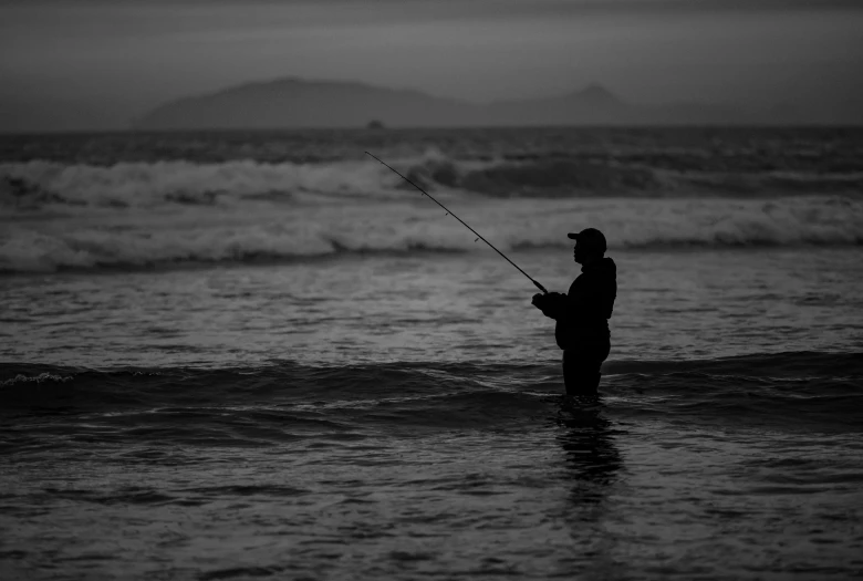 a man standing on a beach in front of a body of water holding a fishing rod