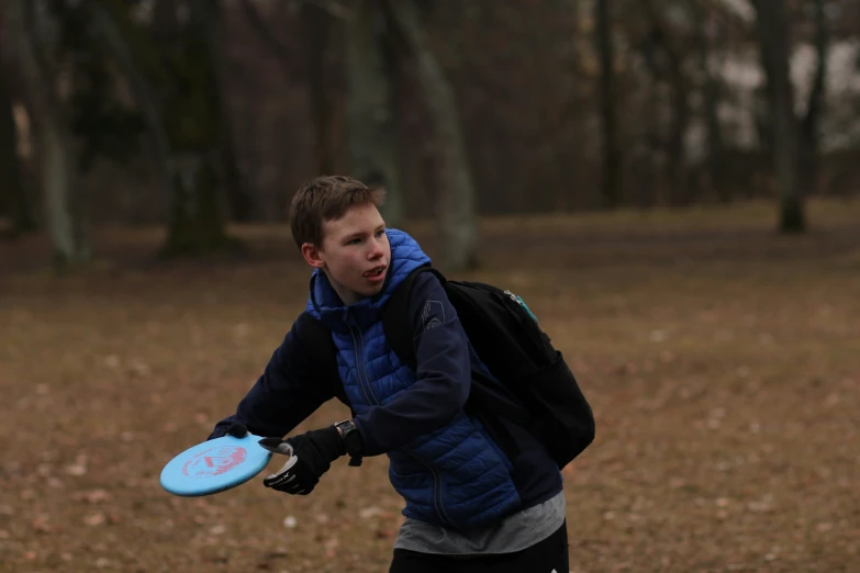 boy playing frisbee in an open field with many trees