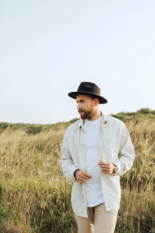 a man in a hat and coat stands near some tall grass