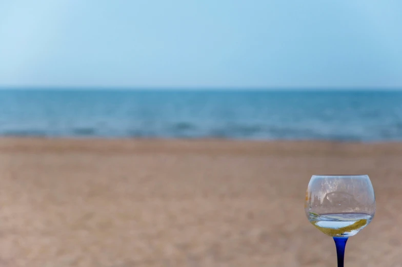 a small wine glass filled with white wine sitting on top of a sandy beach