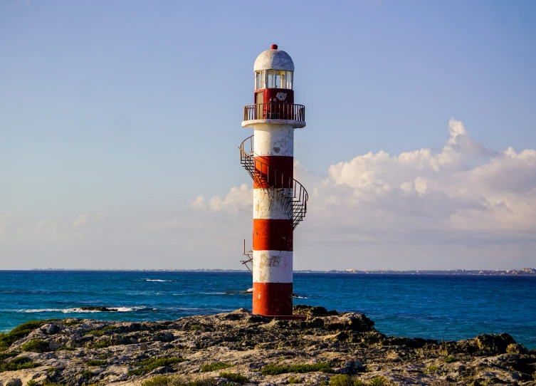 a tall red and white lighthouse sitting on the rocks near the ocean