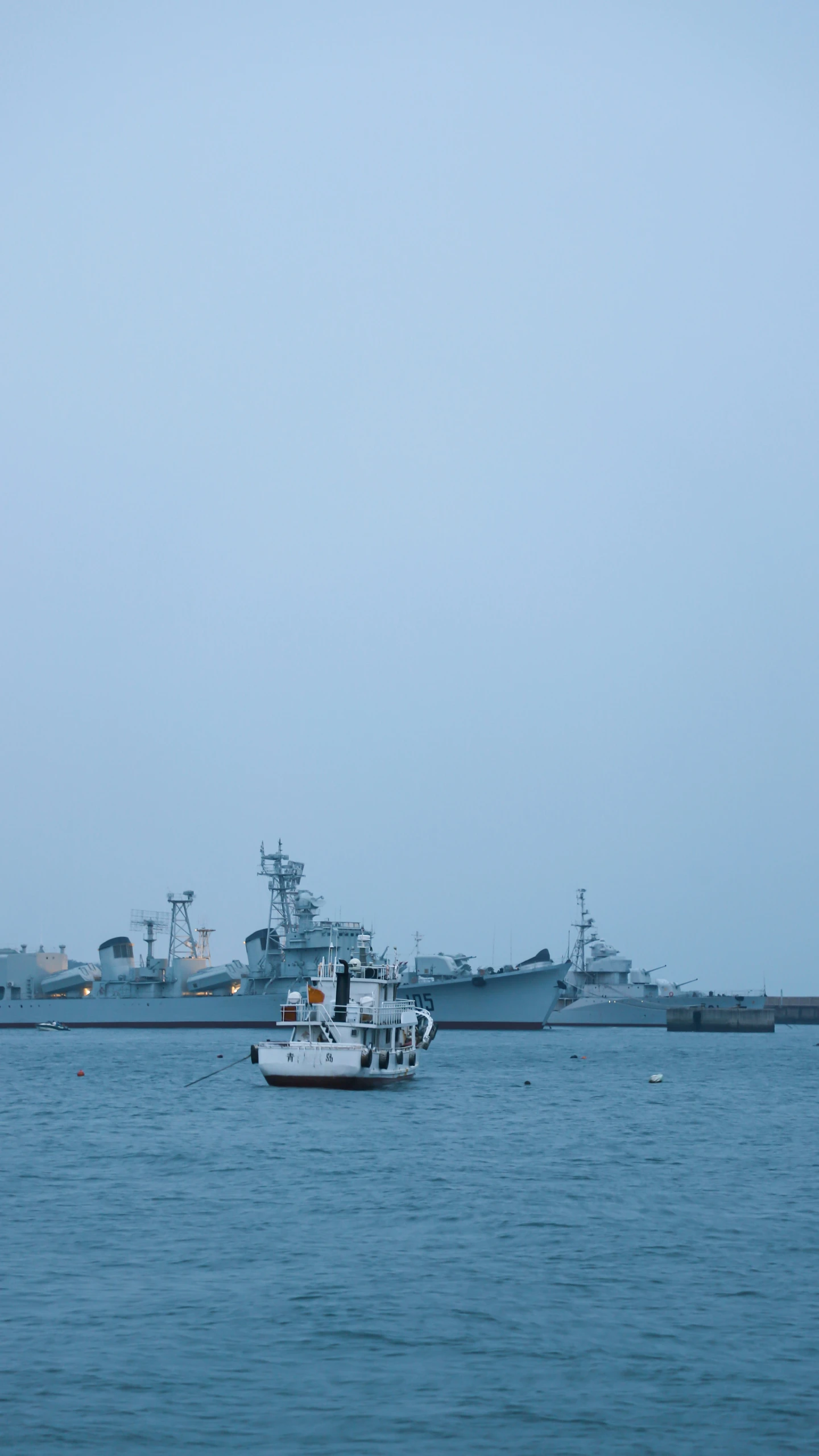 a large navy ship sits near another one in the water