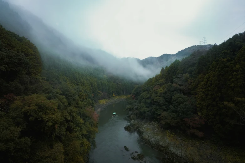 a river flowing down a forested hillside under a foggy sky