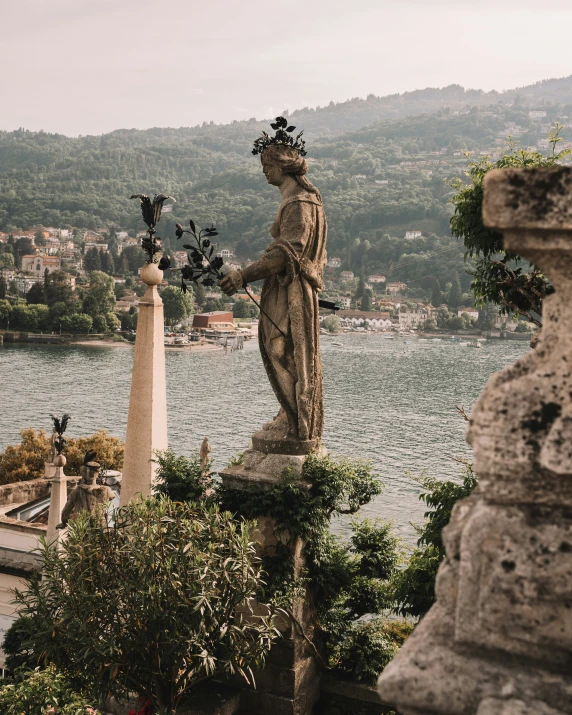 a statue stands next to some water and trees