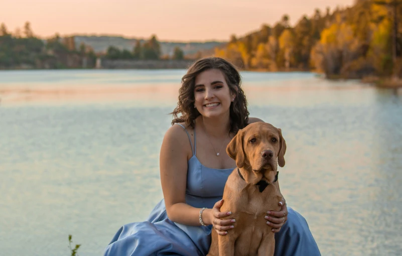 a woman sitting with her dog beside a body of water