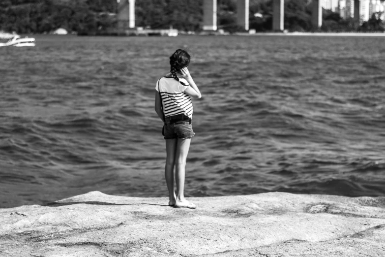 a black and white pograph of a girl looking out over water