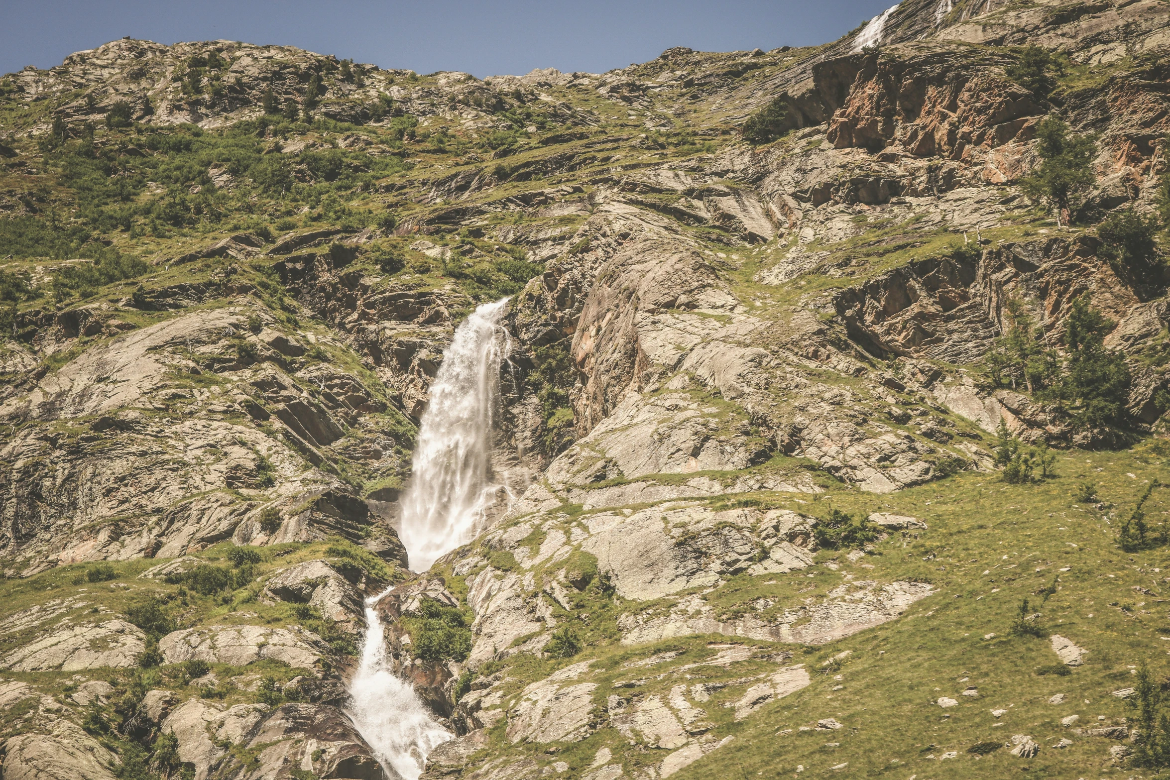 a man is walking along side a mountain with a waterfall in the background