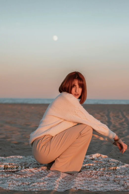 a woman in white sweater sitting on a sand covered ground