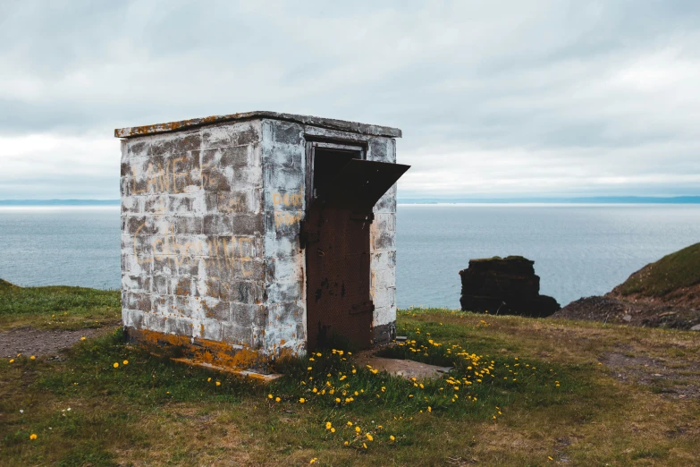 old concrete outhouse standing in the grass near a body of water