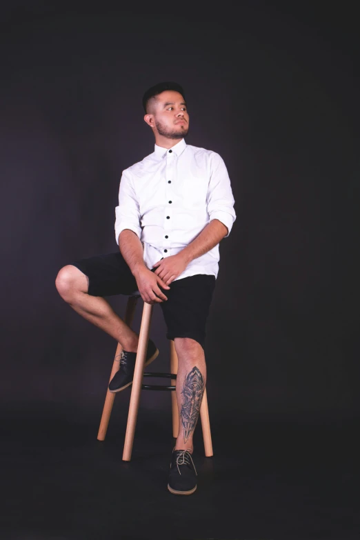 a man in a white shirt and black shorts sitting on a wooden stool