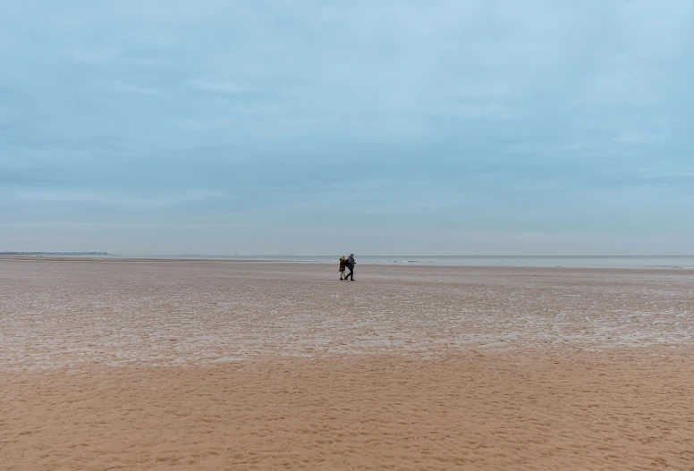 a single man is walking across the sandy beach with a kite in the air