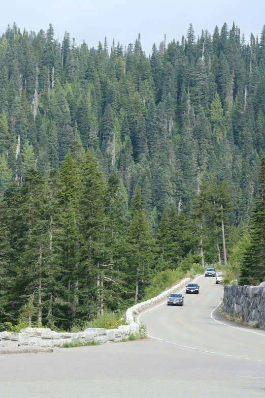 several cars driving down the road by a hillside