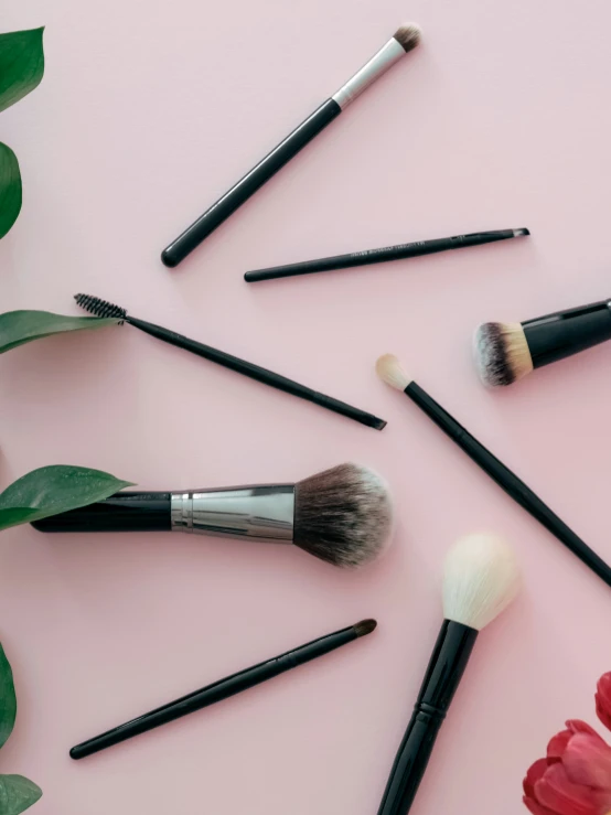 makeup brushes and flowers on a pink surface