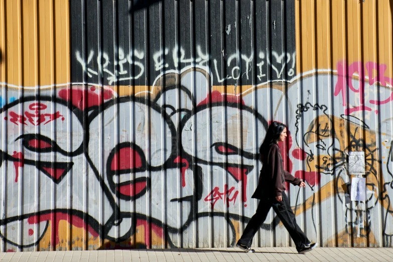 a man walking down a sidewalk past graffiti covered buildings