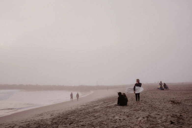 people standing on the beach while they watch a person fly a kite