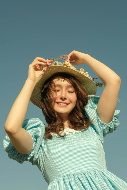a  wearing a green dress holding a brown hat on her head