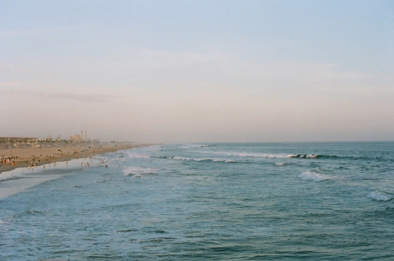 many people are standing on the beach as waves crash on the shoreline