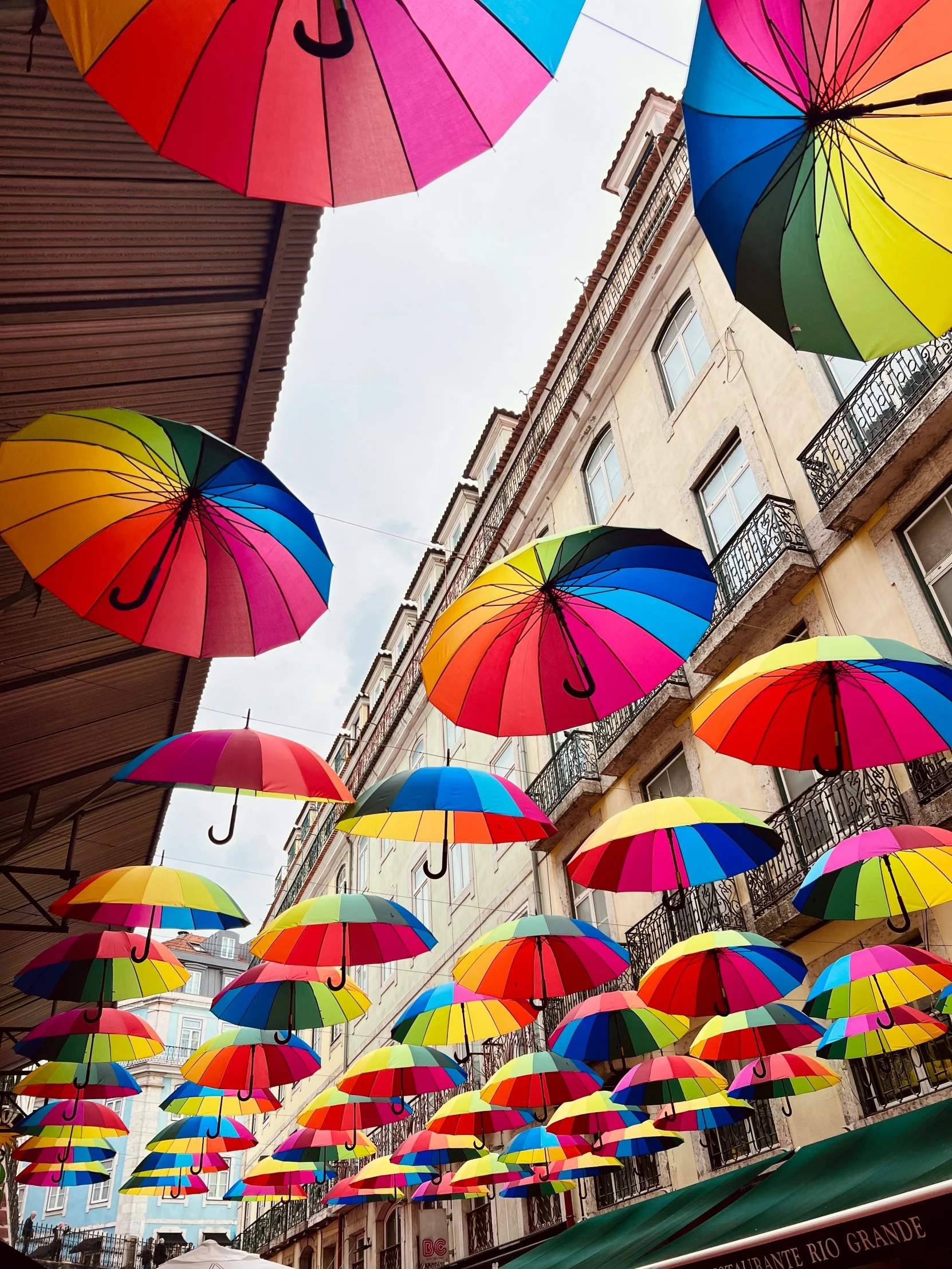 an array of multicolored umbrellas hanging above a city sidewalk