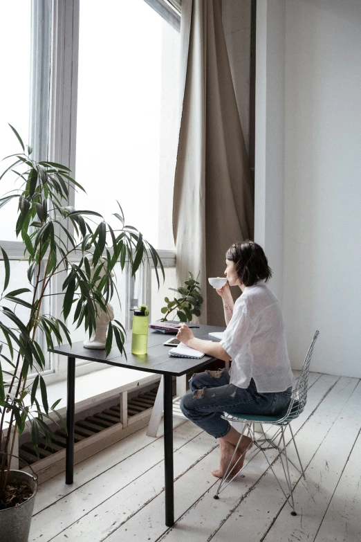 a woman sitting at a table by a window using her laptop