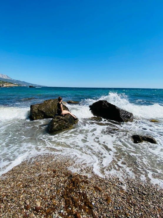 a woman sits on some rocks while she sits next to the water