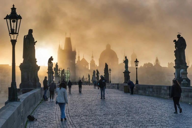 people walking in front of the spires of a building with mist rolling around