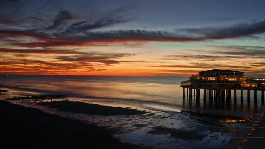 the sun sets over a beach next to a pier