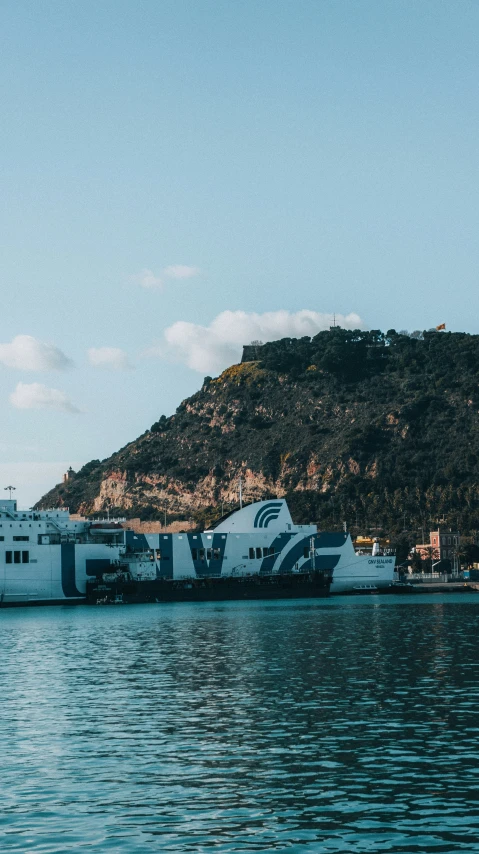 large white boat traveling along side of shore next to mountain