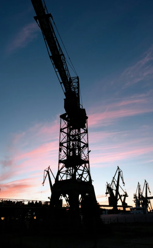 an industrial tower with several cranes sitting in front of the sunset