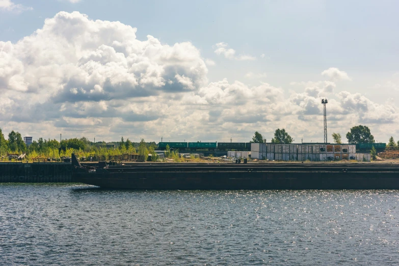 a very long boat in the water, with some buildings and trees behind it