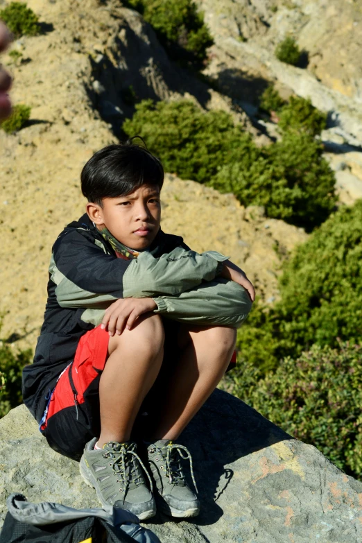 a child sitting on a rock with his back against the camera