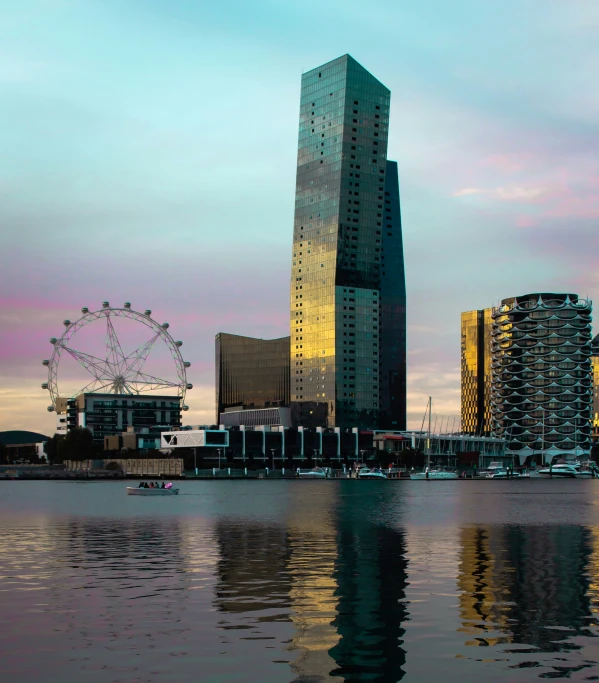 a city sits on the water in front of a ferris wheel