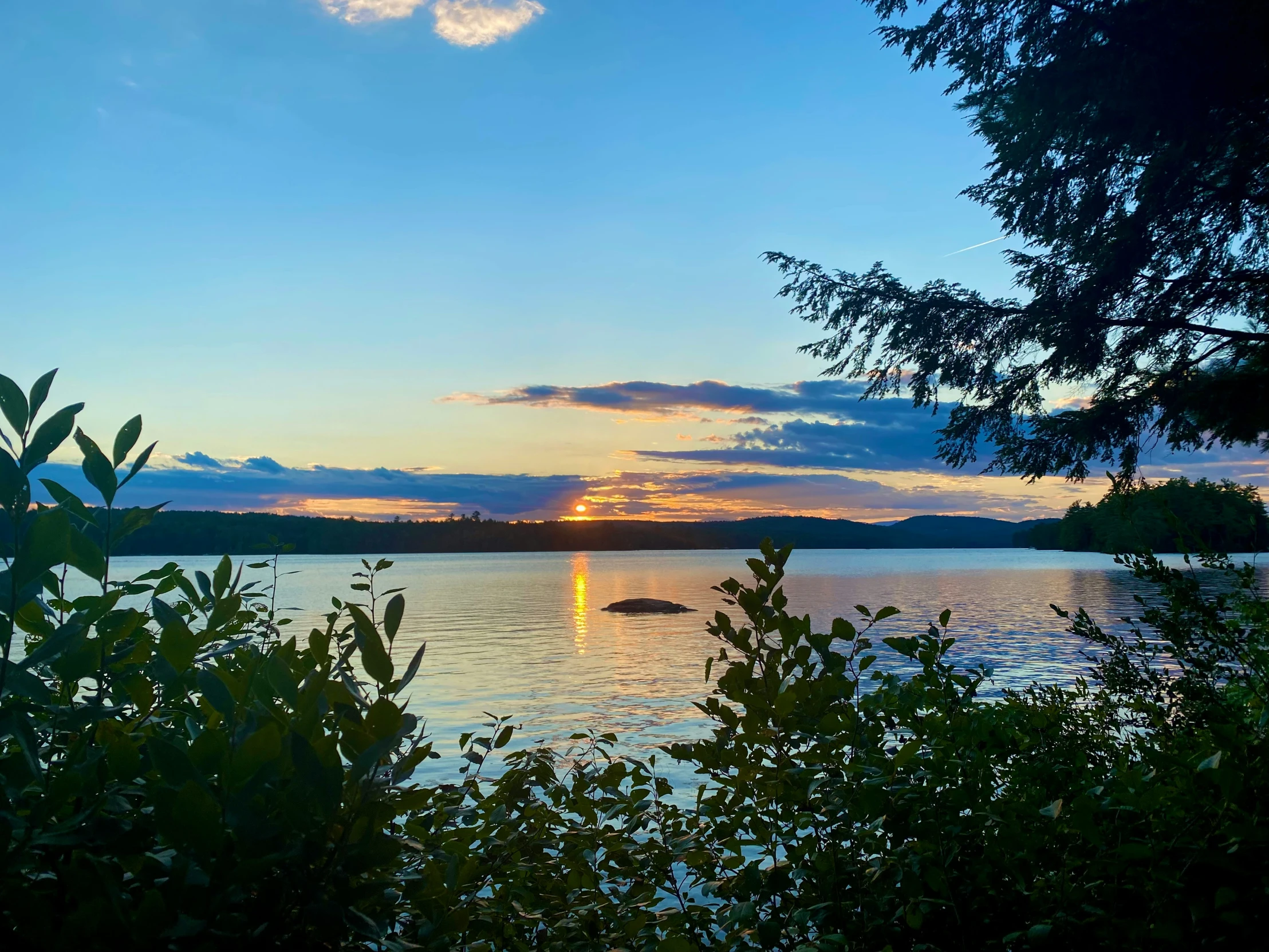 the sun is setting on a lake surrounded by trees