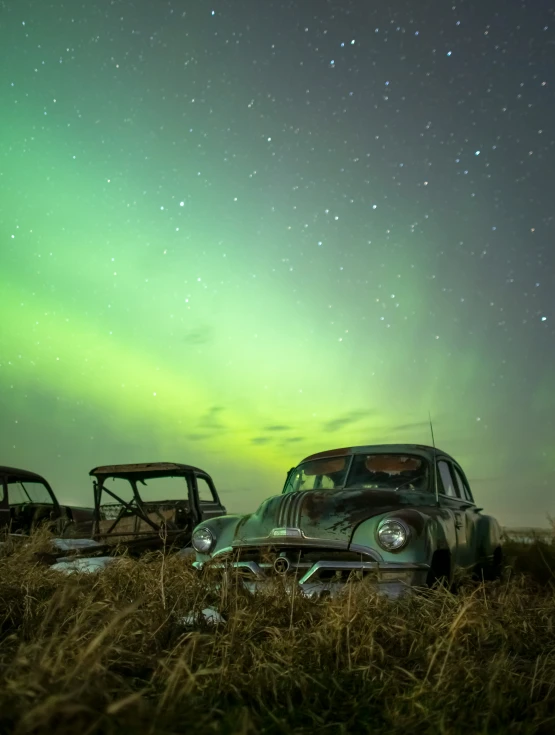 an old car is sitting in a field with the lights from the night sky